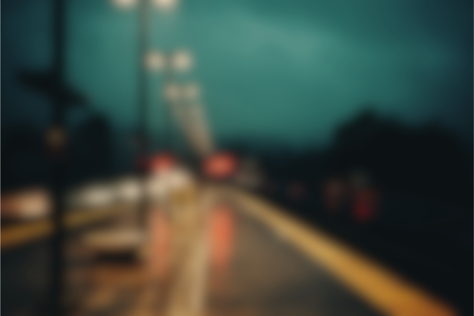 Heavily blurred image of a rainy train platform at night with station lights visible, creating an indistinct and atmospheric scene